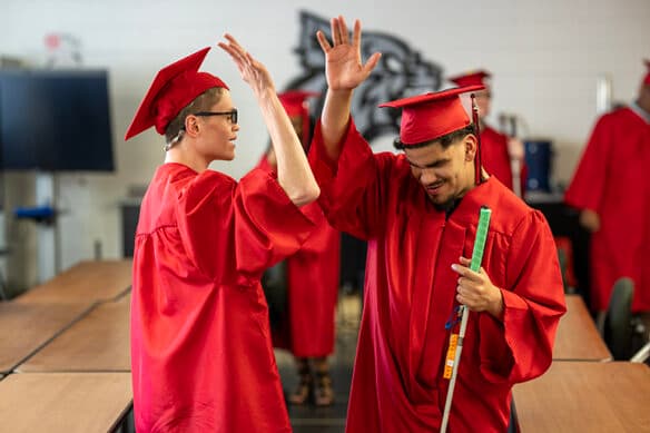 Two students at in red caps and gowns high-fiving at Kentucky School for the Blind's graduation ceremony