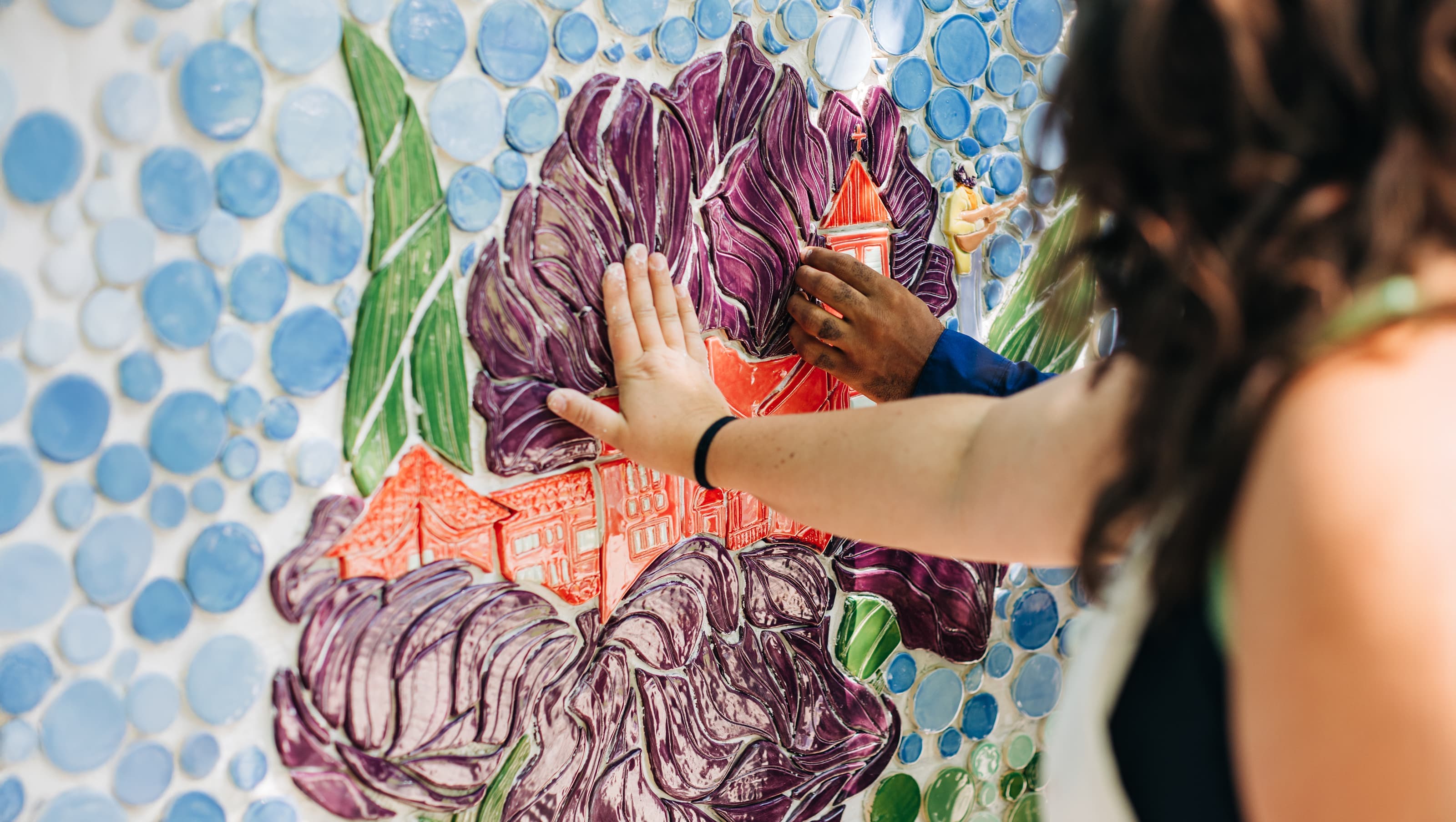 A pair of hands feeling the tile of the Clifton Center surrounded by flowers
