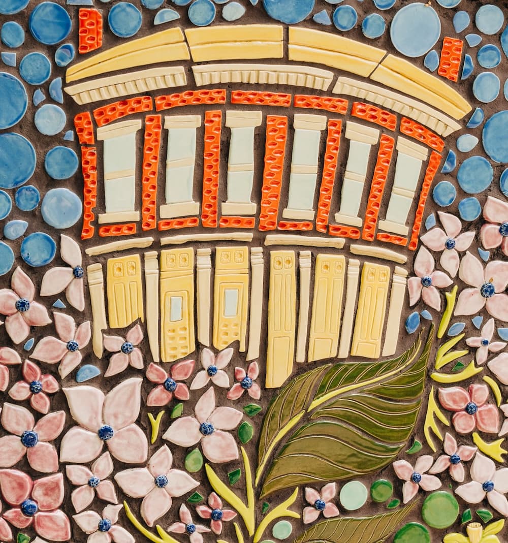 A mosaic panel of the cream-colored historic Irish Rover building with arched windows, surrounded by pale pink flowers