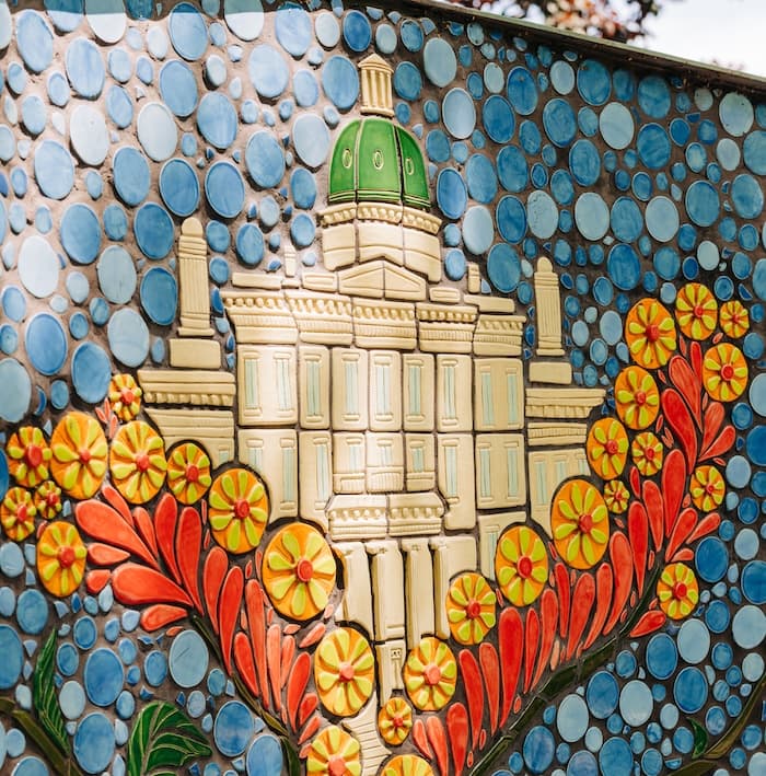 A mosaic panel of the domed neoclassical Kentucky School for the Blind building, framed by red petals and orange starburst flowers on blue tiles